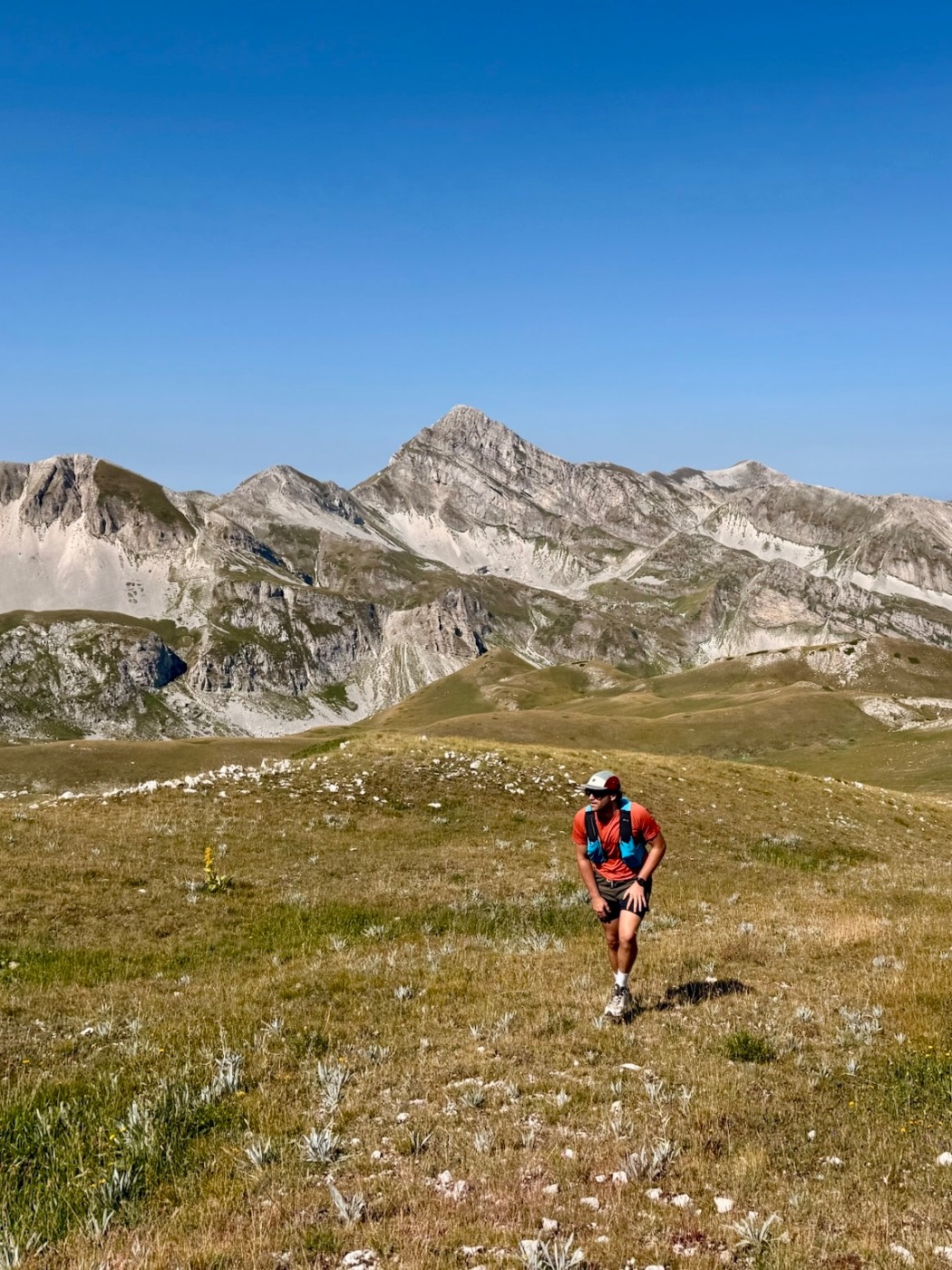 Un escursionista sale su un prato d'alta quota, con una vetta rocciosa sullo sfondo